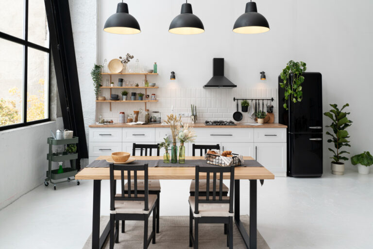 White kitchen with a black fridge, extractor hood and pendant lights, with a wooden dining table