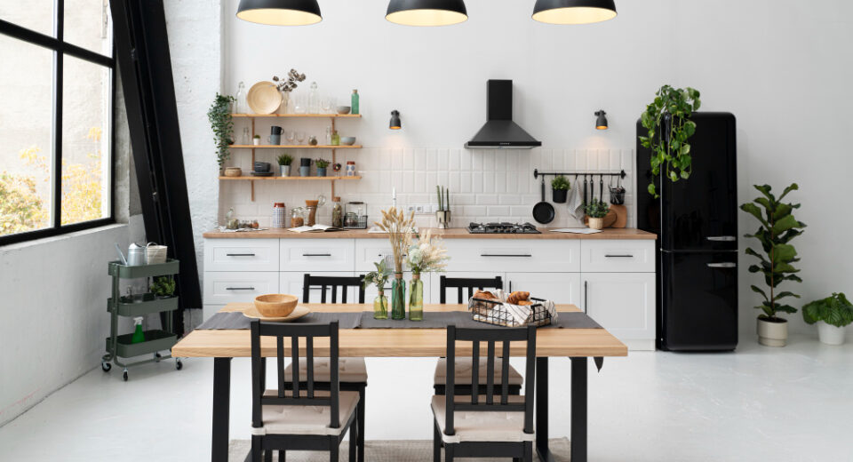 White kitchen with a black fridge, extractor hood and pendant lights, with a wooden dining table